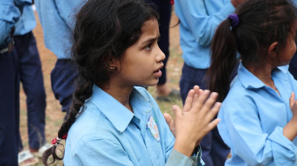 Children in uniforms clapping during an outdoor school activity.